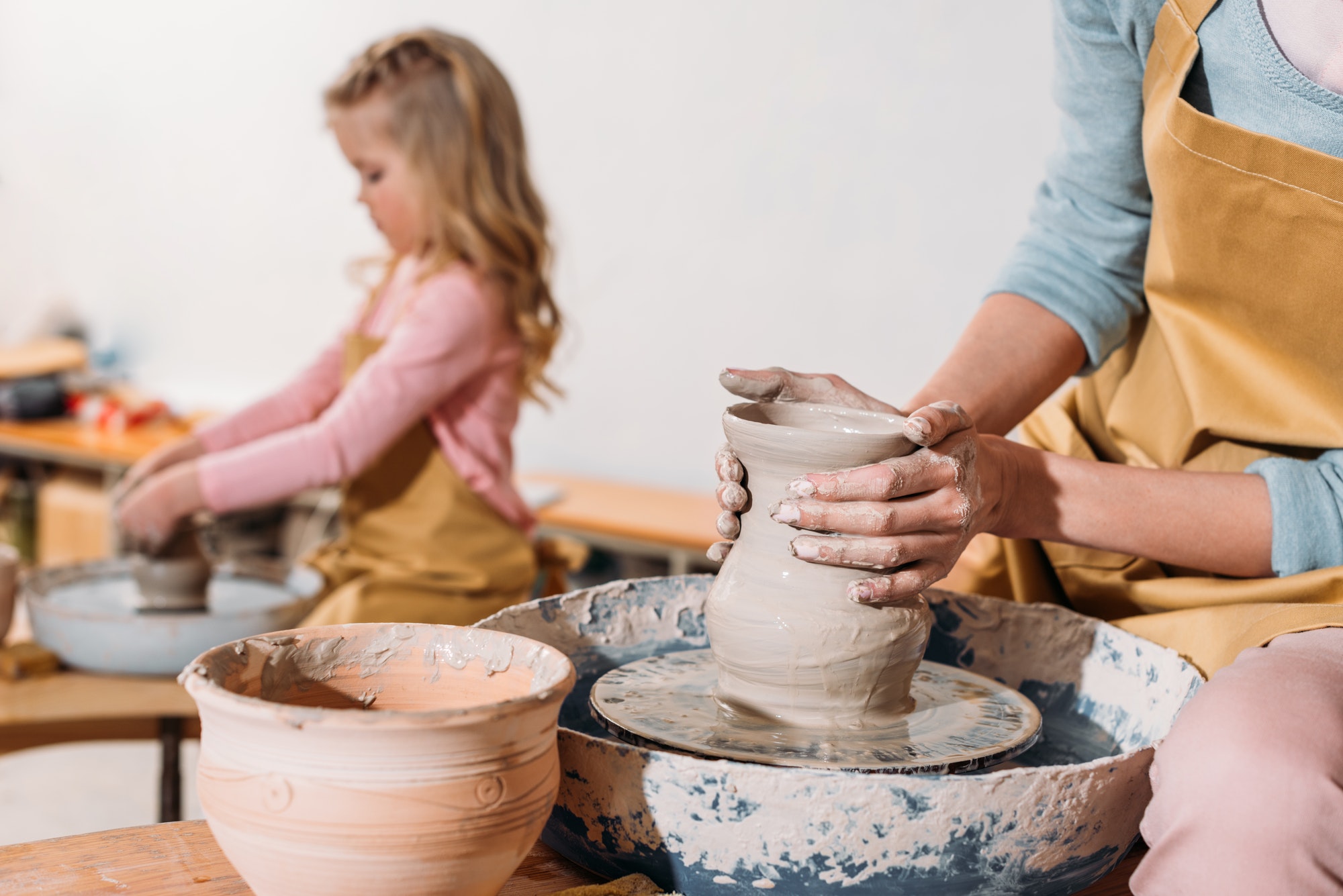 selective-focus-of-daughter-making-ceramic-pot-on-pottery-wheel-with-mother-on-foreground.jpg